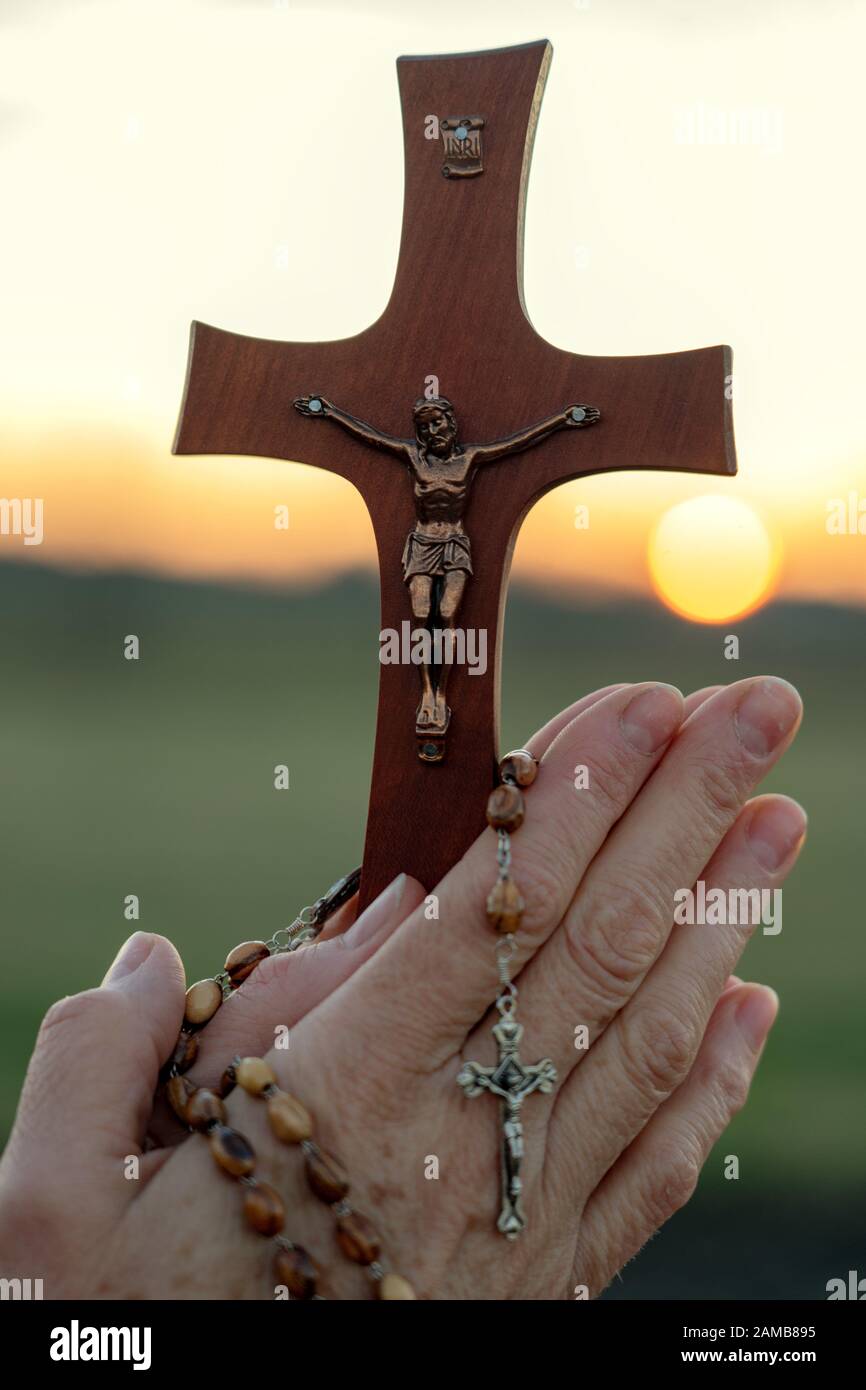 Femme priant en plein air avec un crucifix au coucher du soleil Banque D'Images