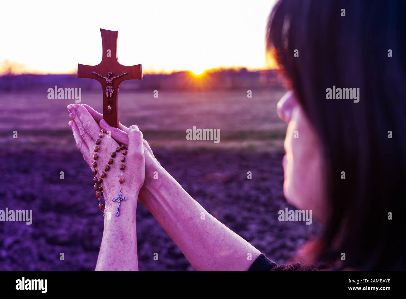 Femme priant en plein air avec un crucifix au coucher du soleil Banque D'Images