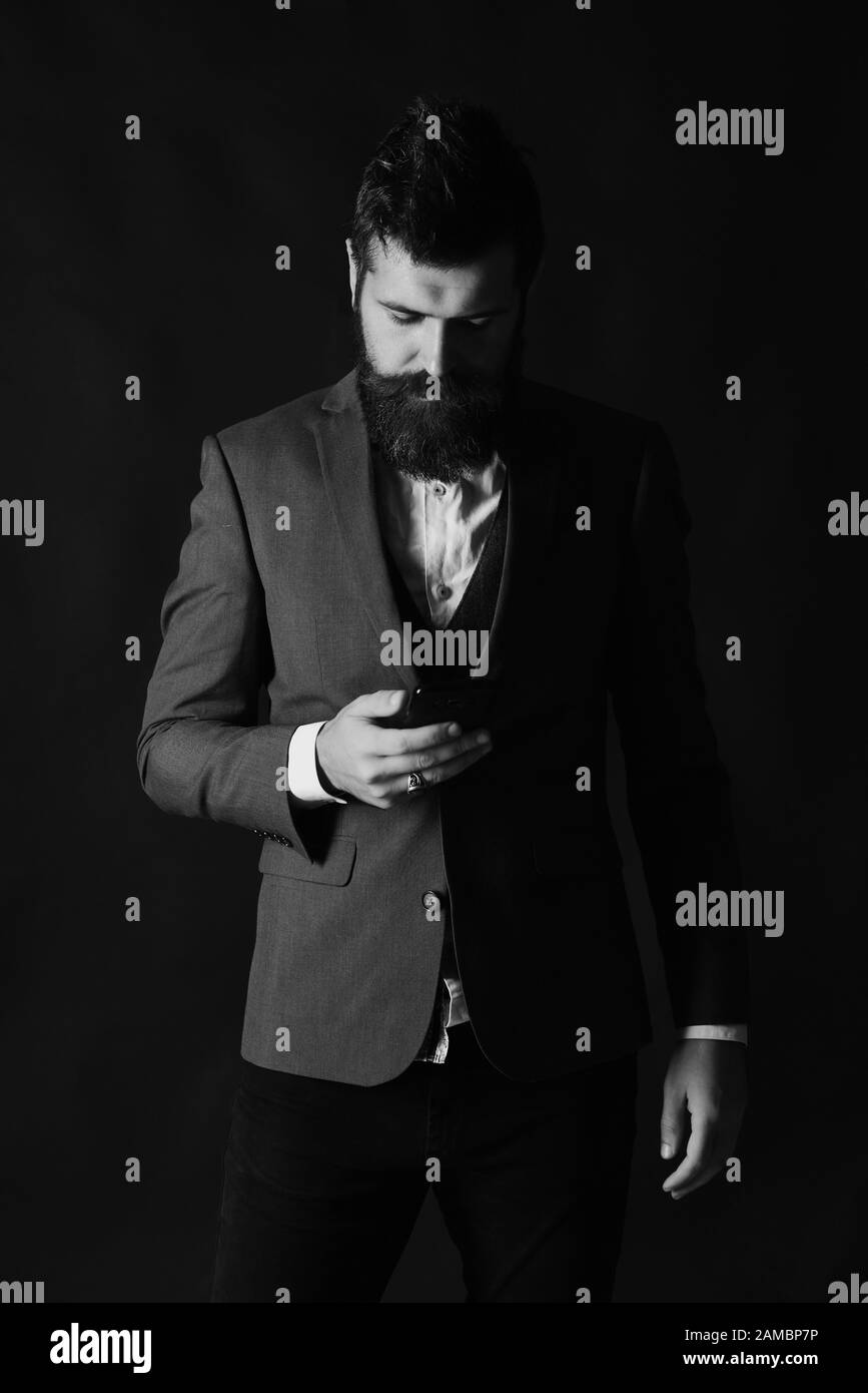 Concept commercial et technologique. Homme d'affaires avec barbe tient le téléphone portable. Homme en costume intelligent types message ou naviguer sur Internet sur fond brun. L'homme avec le visage sérieux utilise le gadget. Banque D'Images