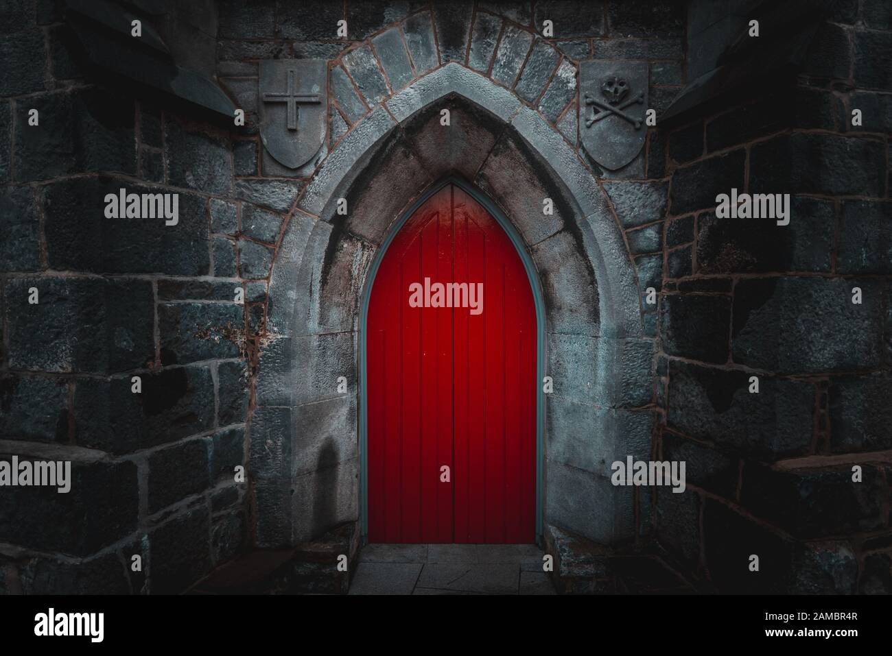 Porte en bois rouge pointu effrayant dans un vieux mur de pierre humide et bâtiment avec cross, du crâne et des os des deux côtés. Mystère, la mort et la notion de danger. Banque D'Images