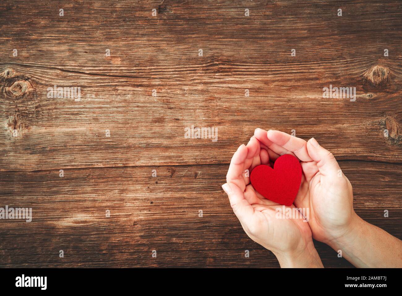 vue de dessus des mains de la femme tenant le cœur rouge sur la table en bois Banque D'Images