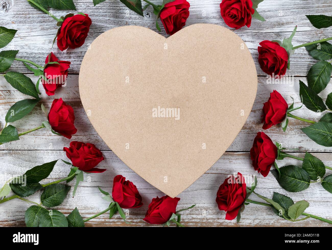 Bonne Saint Valentin avec des roses rouges entourant une boîte cadeau en forme de coeur sur bois rustique blanc Banque D'Images