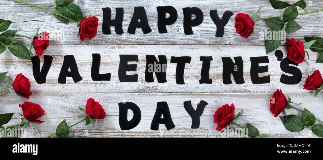 Bonne Saint Valentin avec de grandes lettres entourées de roses rouges sur le bois rustique blanc Banque D'Images