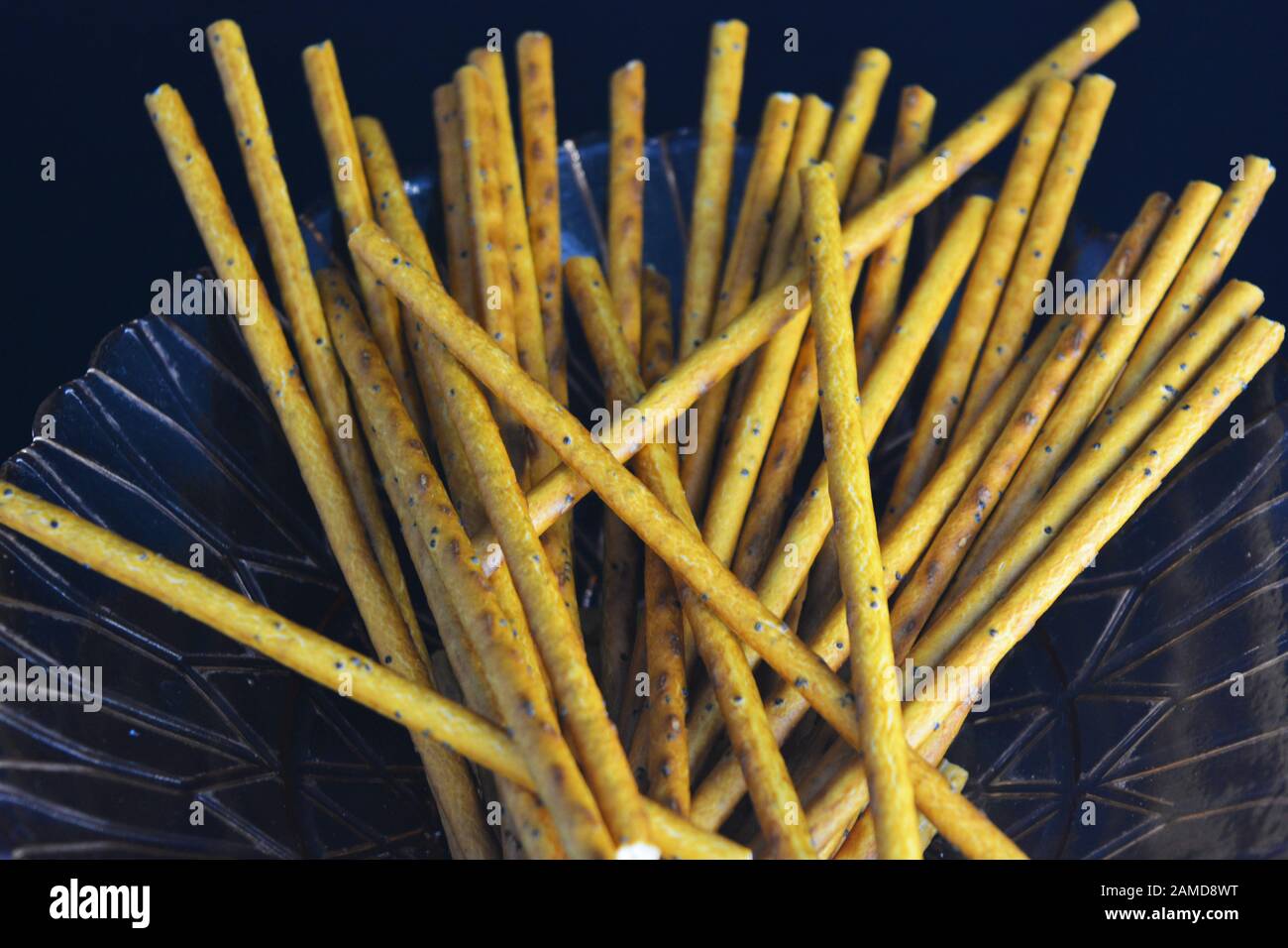 Des pailles savoureuses et sucrées avec des graines de pavot faites de farine, la sneking sont situées dans une plaque de verre marron sur un fond en plastique noir. Banque D'Images