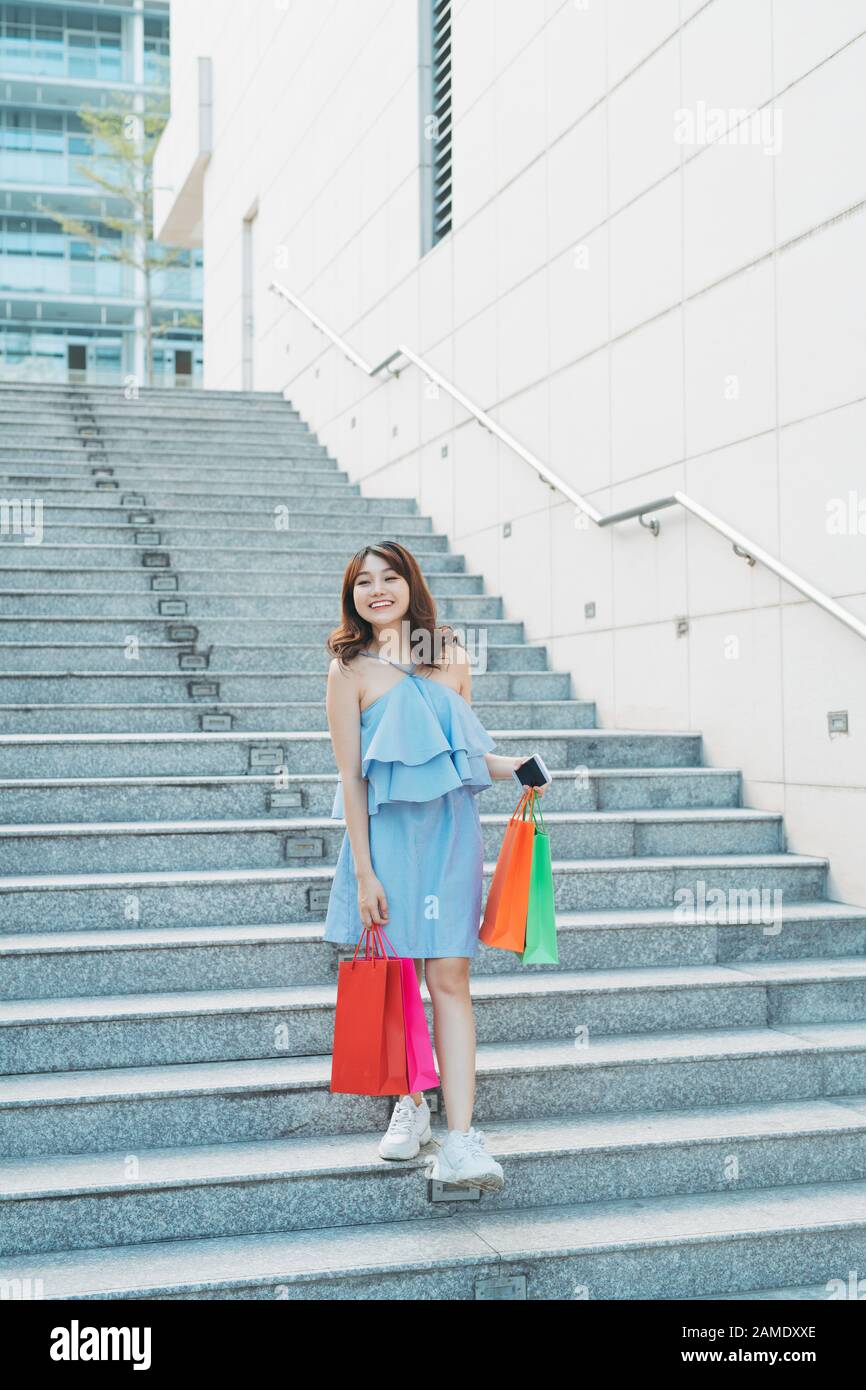 La jeune femme asiatique souriante aime faire du shopping avec un sac coloré tout en descendant les escaliers. Banque D'Images