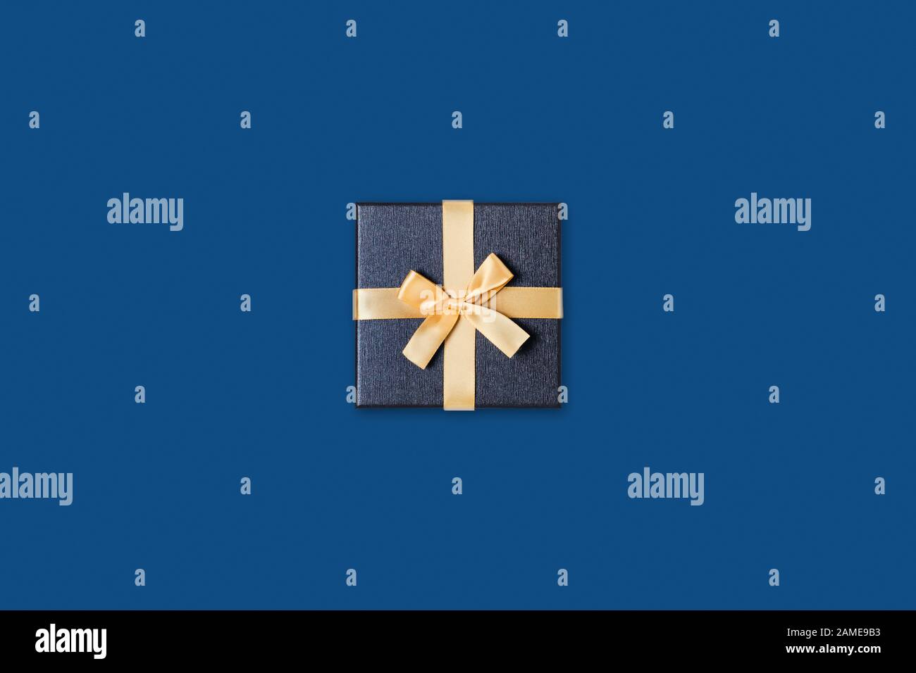 Carte de vacances. Boîte cadeau grise avec noeud doré sur fond bleu classique. Couche plate, vue supérieure, espace de copie. Banque D'Images