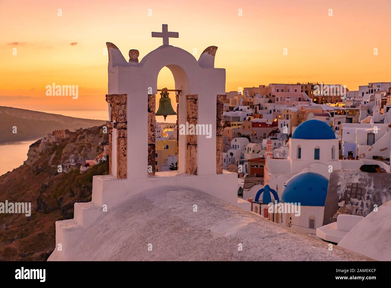 Églises à dôme bleu et clocher face à la mer Égée avec lumière chaude au coucher du soleil à Oia, Santorin, Grèce Banque D'Images