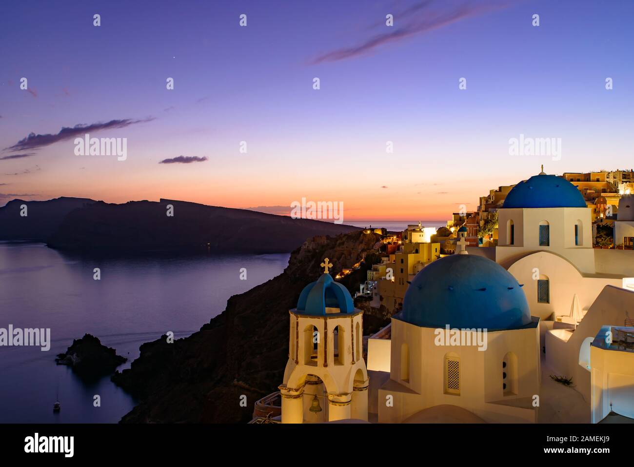 Églises au dôme bleu et maisons blanches traditionnelles face à la mer Égée avec lumière chaude au coucher du soleil à Oia, Santorin, Grèce Banque D'Images