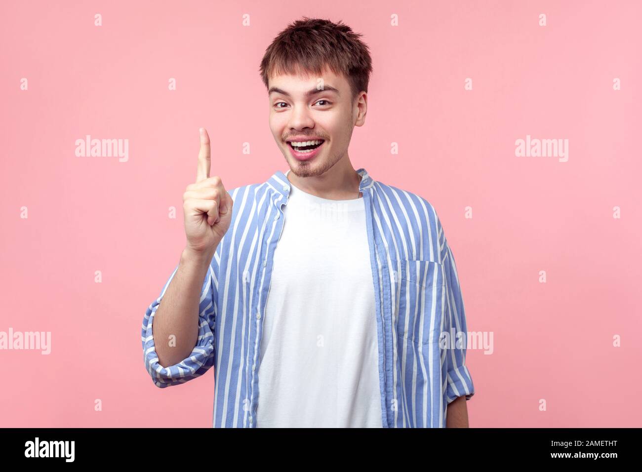 Portrait d'un homme inspiré aux cheveux bruns avec une petite barbe et une moustache dans une chemise à rayures décontractée pointant vers le haut avec un visage heureux, ayant une idée de génie. Dans Banque D'Images