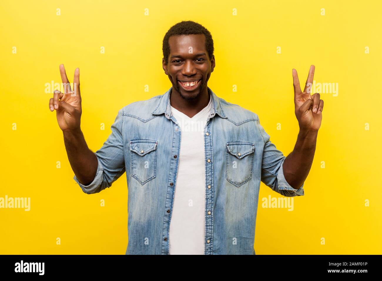 Gagnant réussi. Portrait d'un homme excité avec un sourire toothy dans une chemise denim décontractée debout avec des mains levées et montrant le signe v ou la paix, la victoire ges Banque D'Images