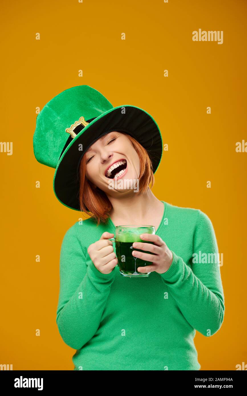 Une femme heureuse avec la bière à boire de chapeau de leprechaun Banque D'Images