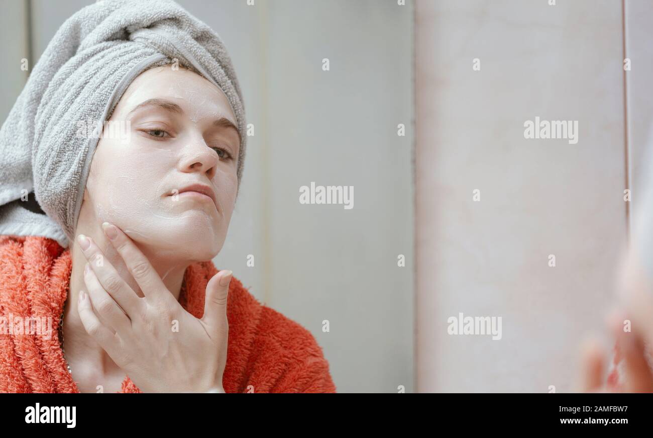 Belle jeune fille heureuse frottant son visage avec un masque cosmétique maison, regardant dans le miroir. Peau et soins de santé, concept de produits naturels écologiques. P Banque D'Images