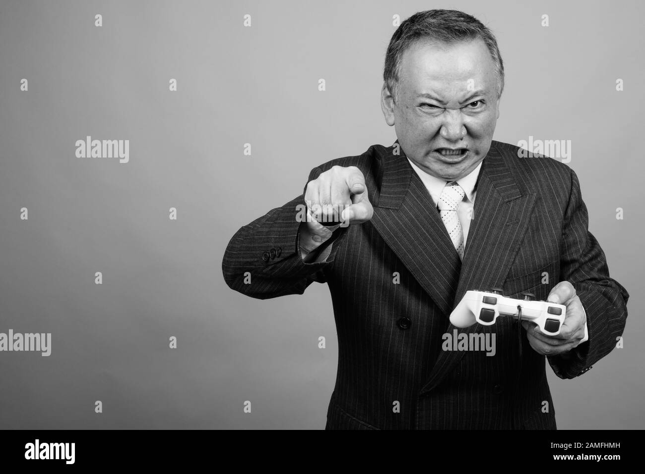 Studio tourné d'un homme d'affaires asiatique mûr jouant à des jeux sur fond gris en noir et blanc Banque D'Images Studio tourné d'un homme d'affaires asiatique mûr jouant à des jeux sur fond gris en noir et blanc Banque D'Images