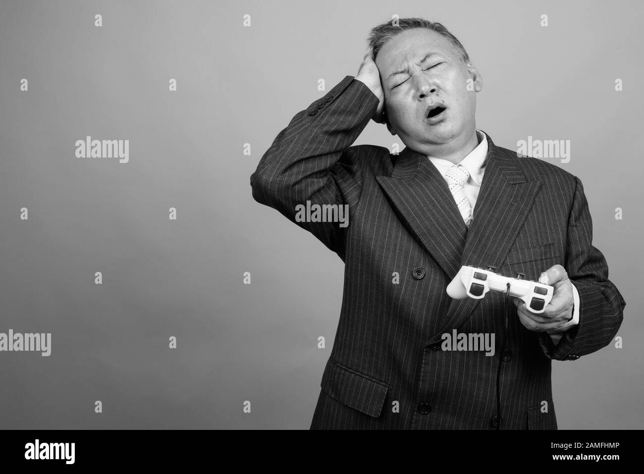 Studio tourné d'un homme d'affaires asiatique mûr jouant à des jeux sur fond gris en noir et blanc Banque D'Images Studio tourné d'un homme d'affaires asiatique mûr jouant à des jeux sur fond gris en noir et blanc Banque D'Images