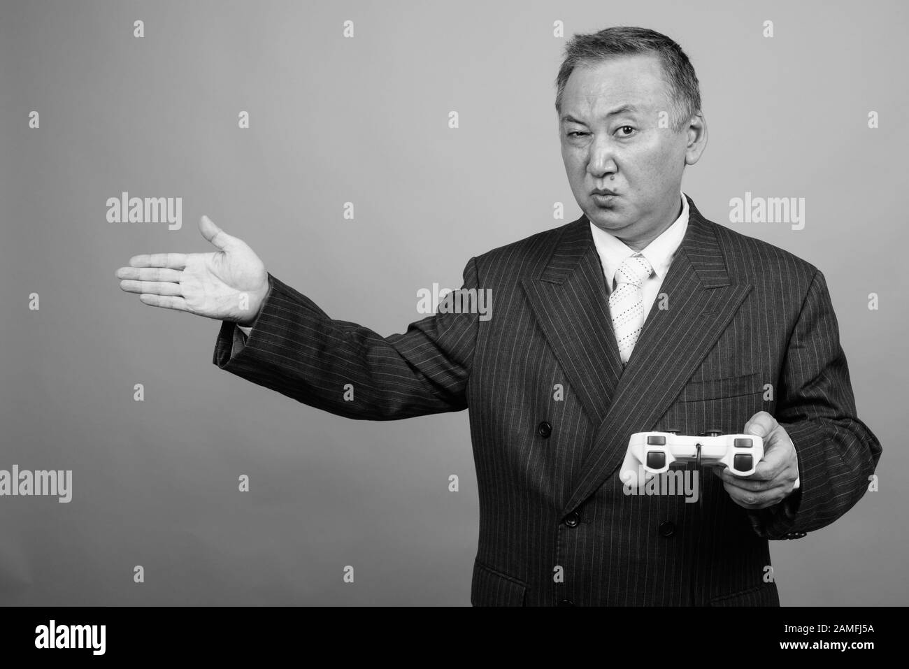 Studio tourné d'un homme d'affaires asiatique mûr jouant à des jeux sur fond gris en noir et blanc Banque D'Images Studio tourné d'un homme d'affaires asiatique mûr jouant à des jeux sur fond gris en noir et blanc Banque D'Images