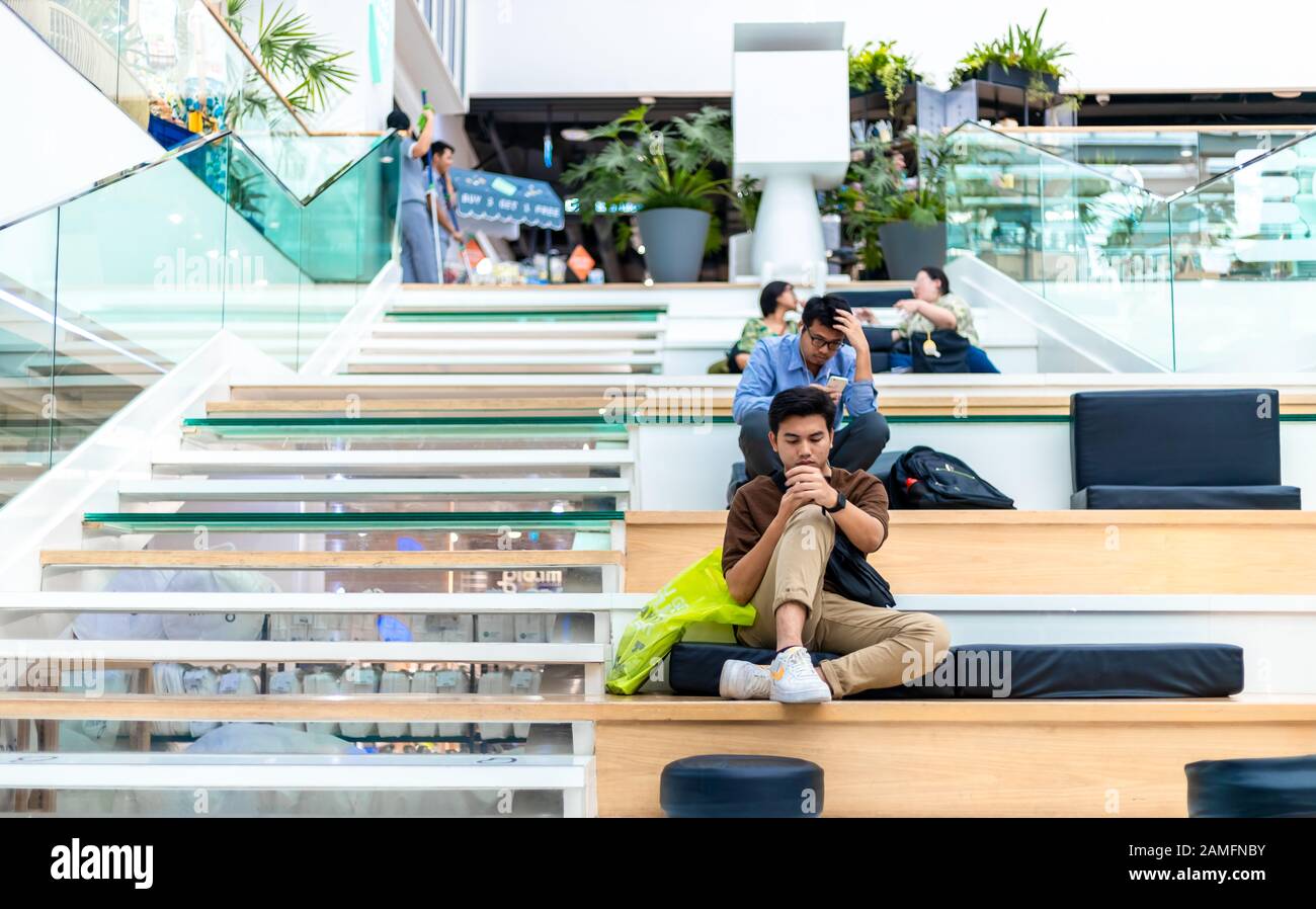 Bangkok, Thaïlande - 28 novembre 2019 : piétons fatigué assis sur le côté des escaliers à l'intérieur du centre commercial Central World à Bangkok. Banque D'Images