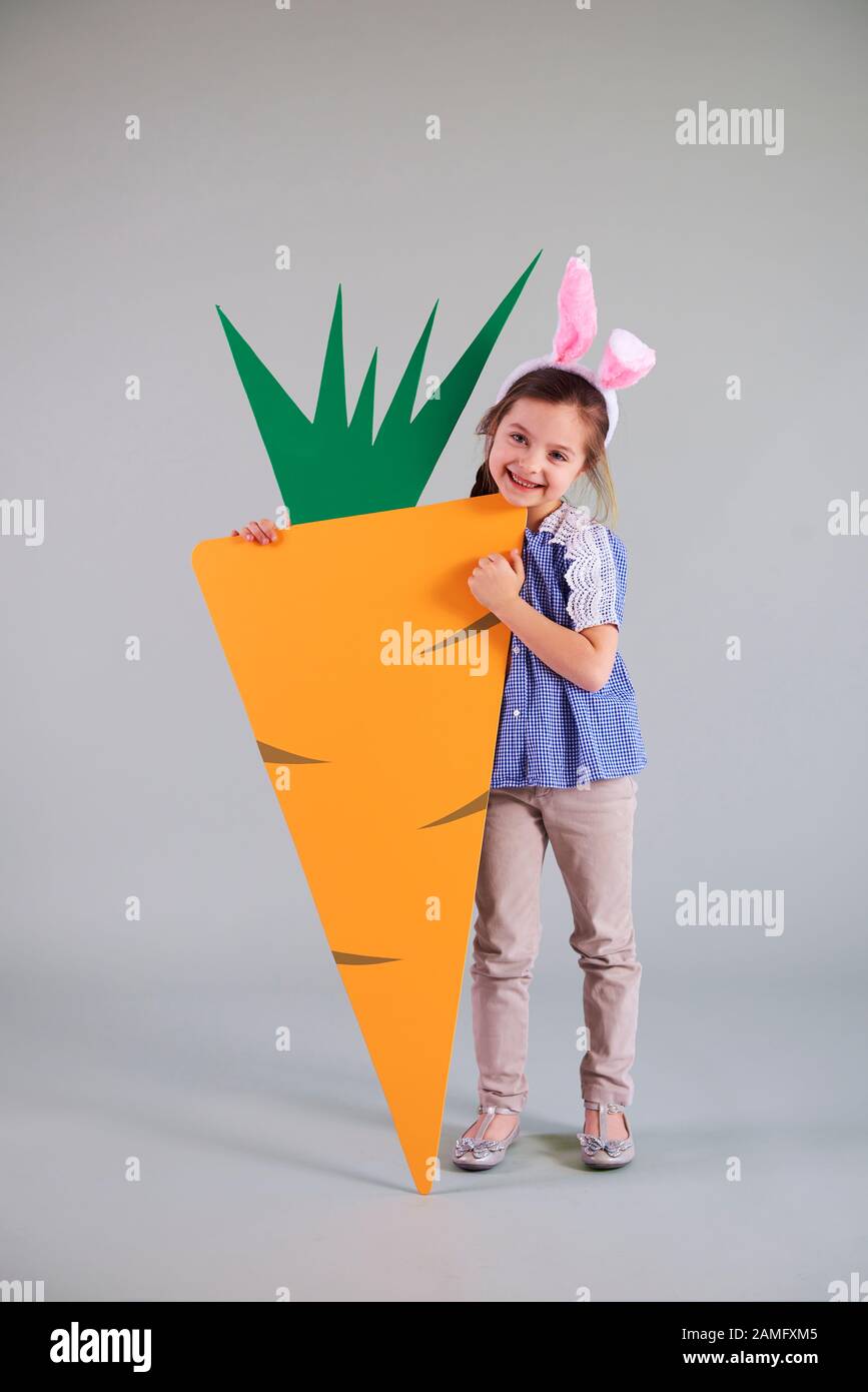 Portrait de l'enfant en costume de lapin de pâques tenant une grosse carotte Banque D'Images