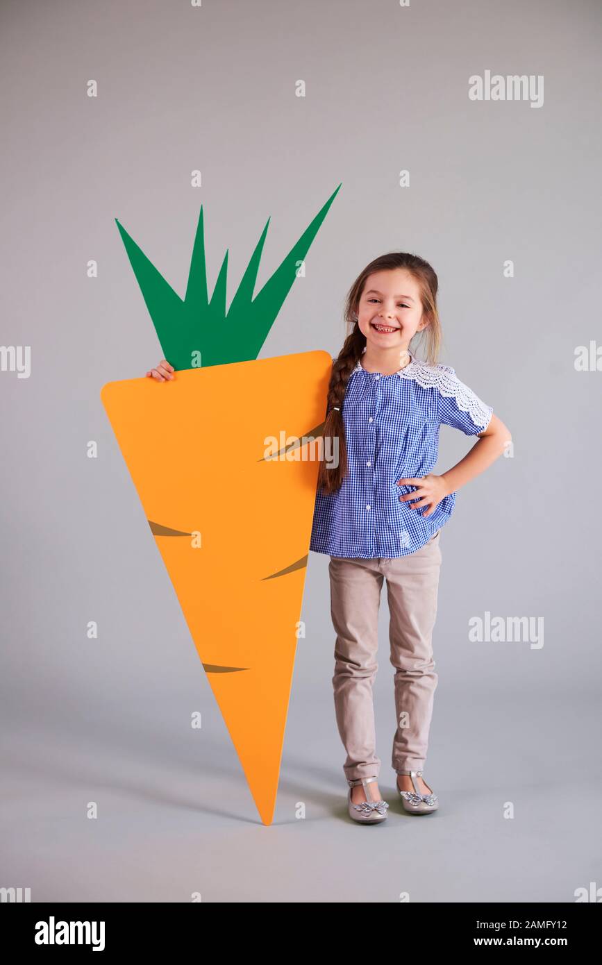 Une fille souriante tenant une grosse carotte artificielle en studio Banque D'Images