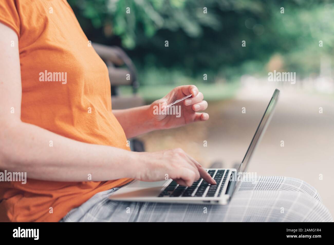 Shopping en ligne dans le parc, femme utilisant ordinateur portable et carte de crédit à l'extérieur Banque D'Images