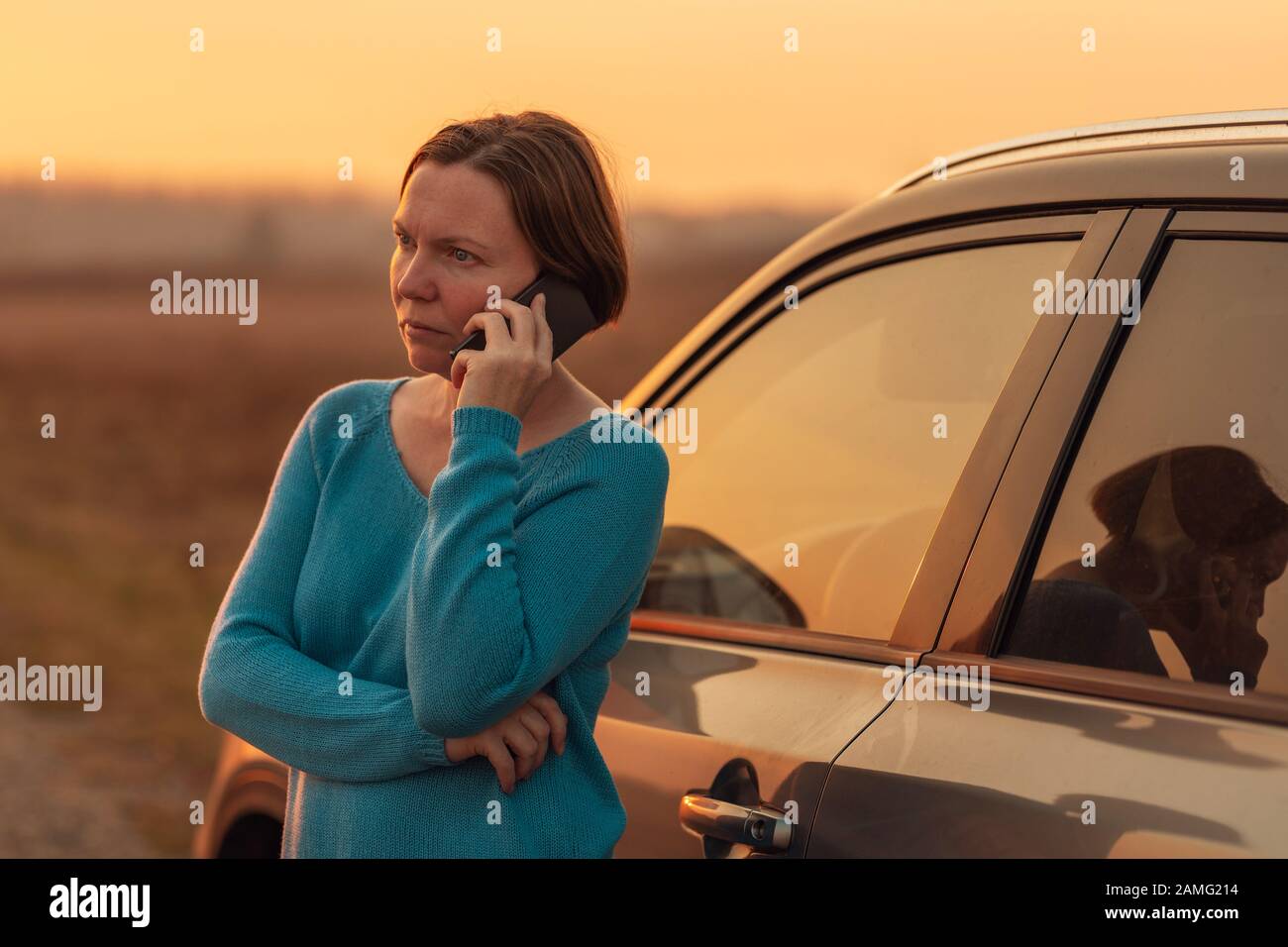 Femme appelant sur téléphone mobile pour l'assistance et l'aide sur la route après sa voiture est tombé en panne en automne coucher du soleil sur la route à travers la campagne, foc sélective Banque D'Images