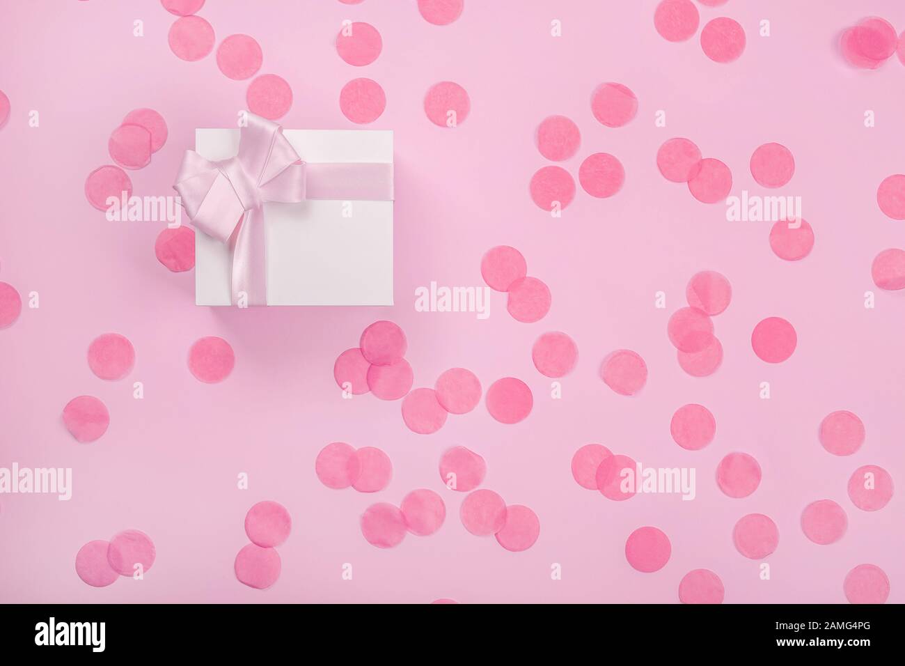 Boîte cadeau avec noeud rose et confettis dispersés autour Banque D'Images