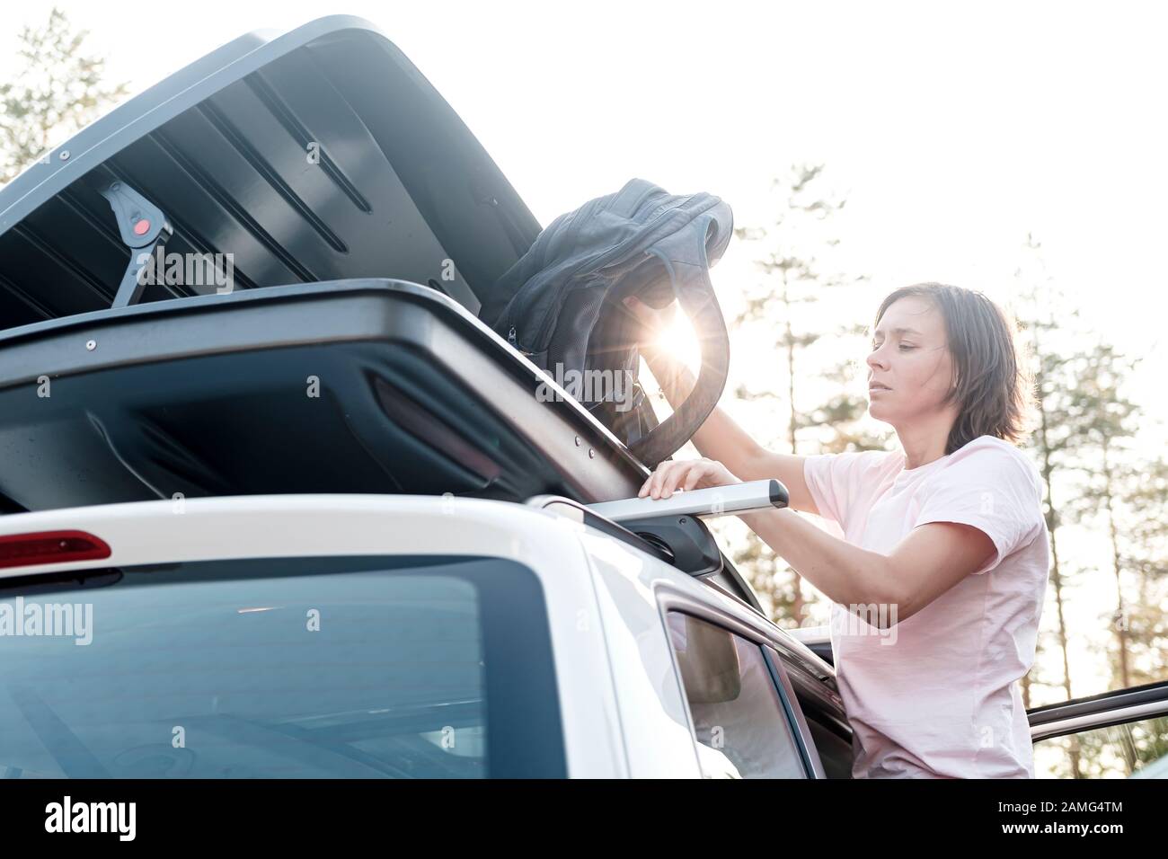 Une femme sérieuse et ciblée place les choses dans le coffre sur le toit d'une voiture ou dans une boîte de chargement. Préparation pour des vacances en famille. Banque D'Images