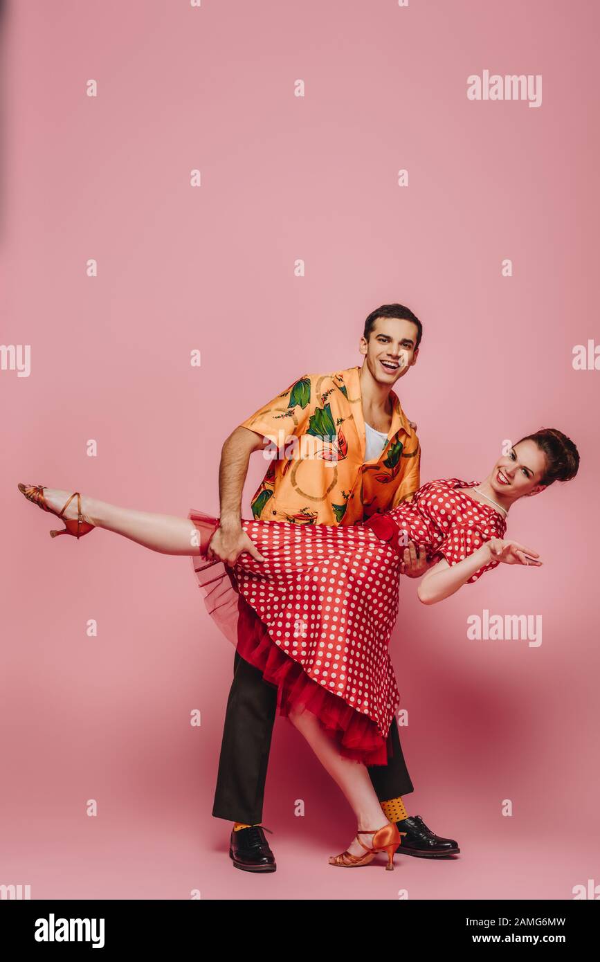 danseuse élégante soutenant partenaire tout en dansant boogie-woogie sur fond rose Banque D'Images