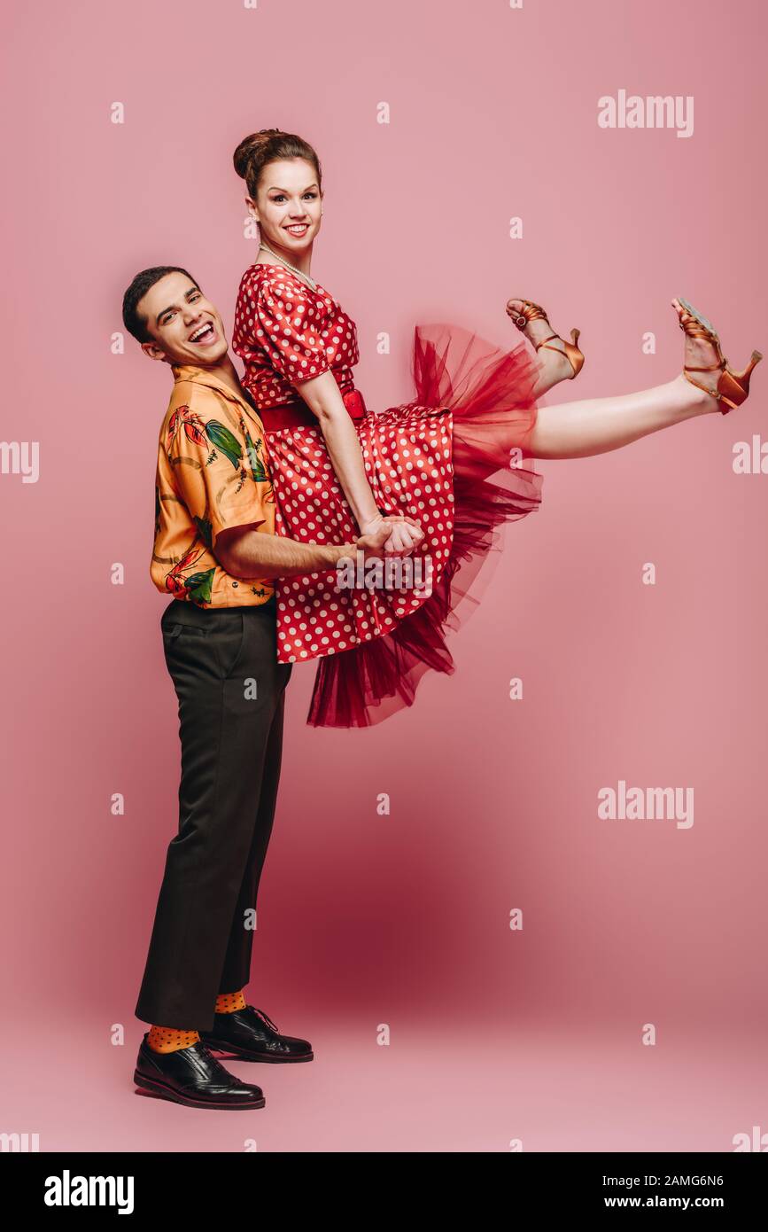 homme élégant tenant la femme tout en dansant la boogie-woogie sur fond rose Banque D'Images