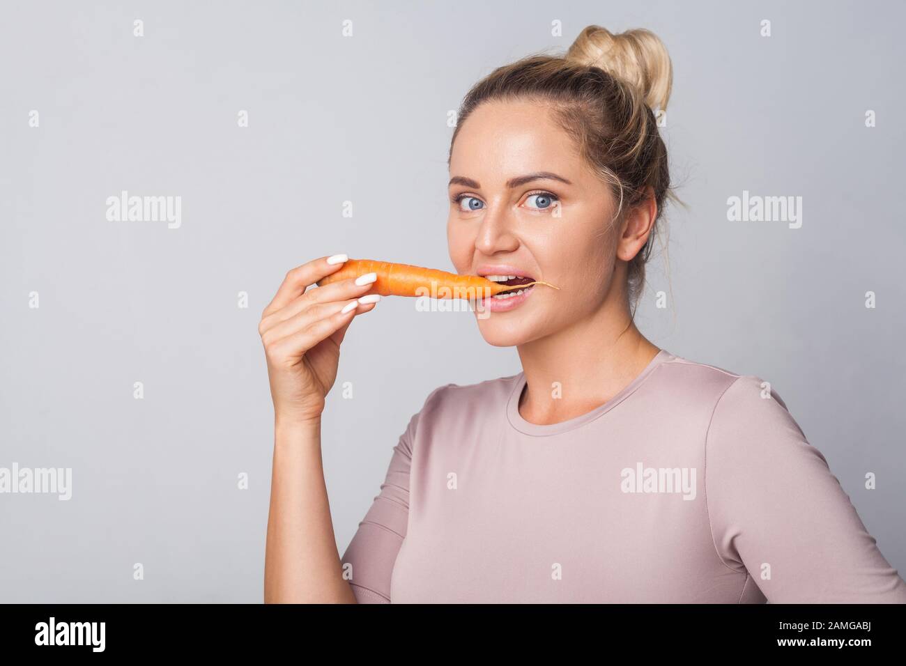 Portrait de la jeune femme mordant la carotte orange, les légumes frais crus, le concept de saine alimentation avec des vitamines bêta-carotène, régime végétarien, faible calori Banque D'Images