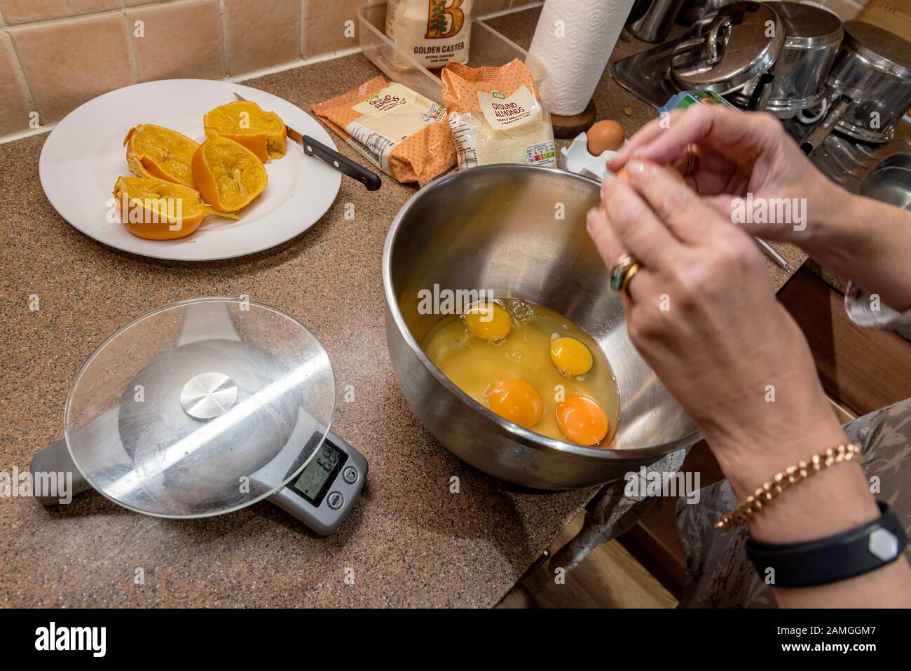 Paire de mains mélangeant un mélange de gâteau avec des œufs dans un bol avec des oranges et des amandes. Banque D'Images
