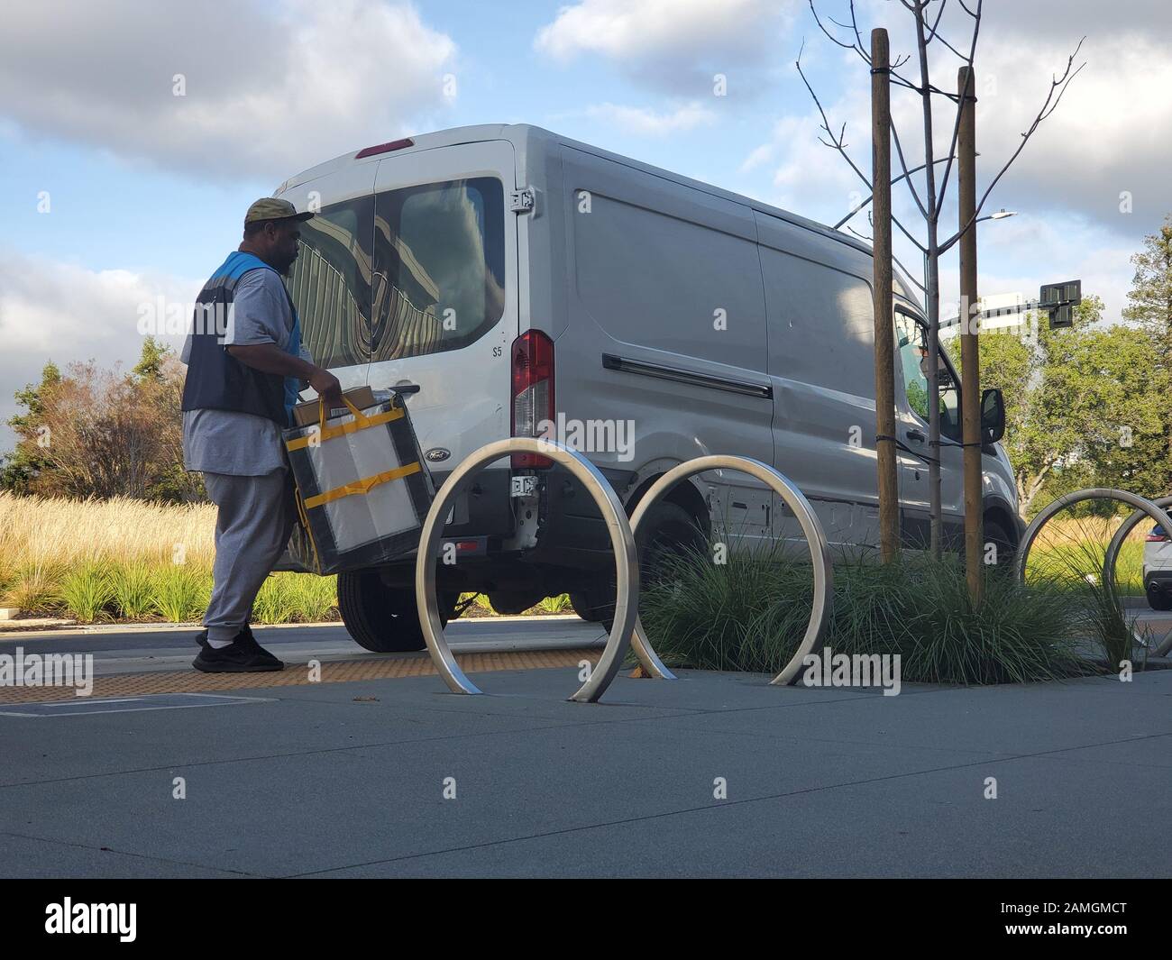 Vue à bas angle d'un livrant portant un gilet avec le logo Amazon déchargeant des paquets pour la livraison d'une camionnette blanche non marquée dans un parc de bureaux à San Ramon, Californie, 19 décembre 2019. () Banque D'Images