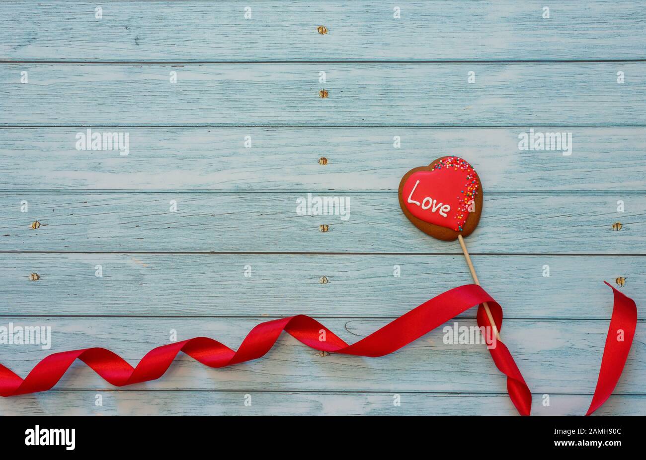 Cookie en forme de coeur décoré sur un bâton avec ruban rouge sur fond bleu en bois. Espace pour le texte. Concept Saint Valentin. Amour Banque D'Images