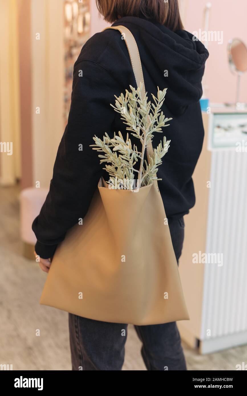 Une fille dans un costume noir et un sac avec un cabas sur son épaule.  Plante verte dans un shoppers beige. Fille à la mode dans un centre  commercial Photo Stock -