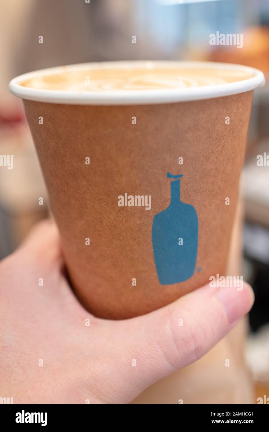 Main d'un homme tenant une tasse à café jetable avec logo bleu devant le nouveau café café à la bouteille de Santana Row shopping mall dans la Silicon Valley, San Jose, Californie, le 12 décembre 2019. () Banque D'Images