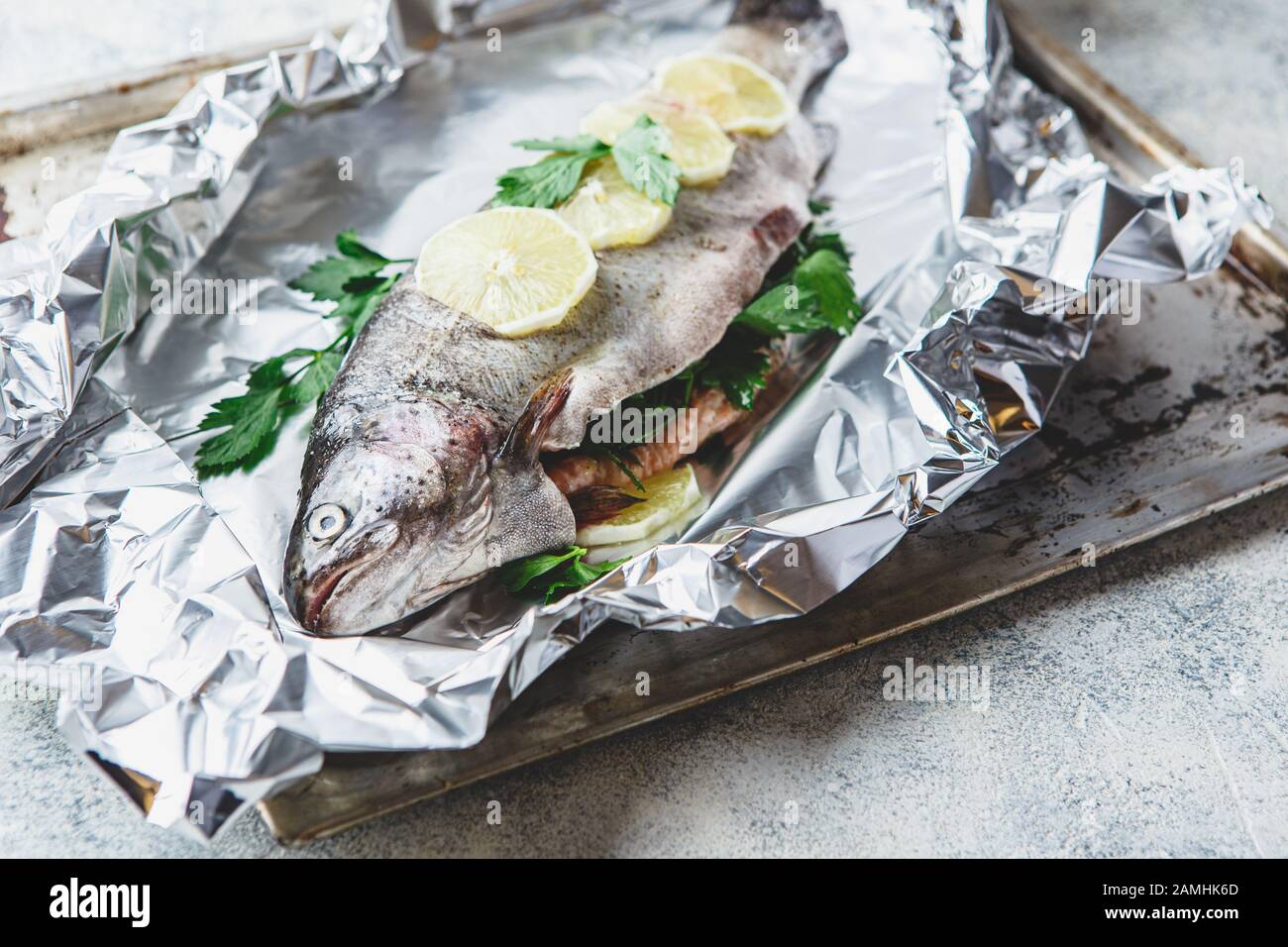 Truite arc-en-ciel fraîche avec persil et citron en feuille d'aluminium sur fond gris clair. Des aliments sains. Concept de cuisson. Banque D'Images