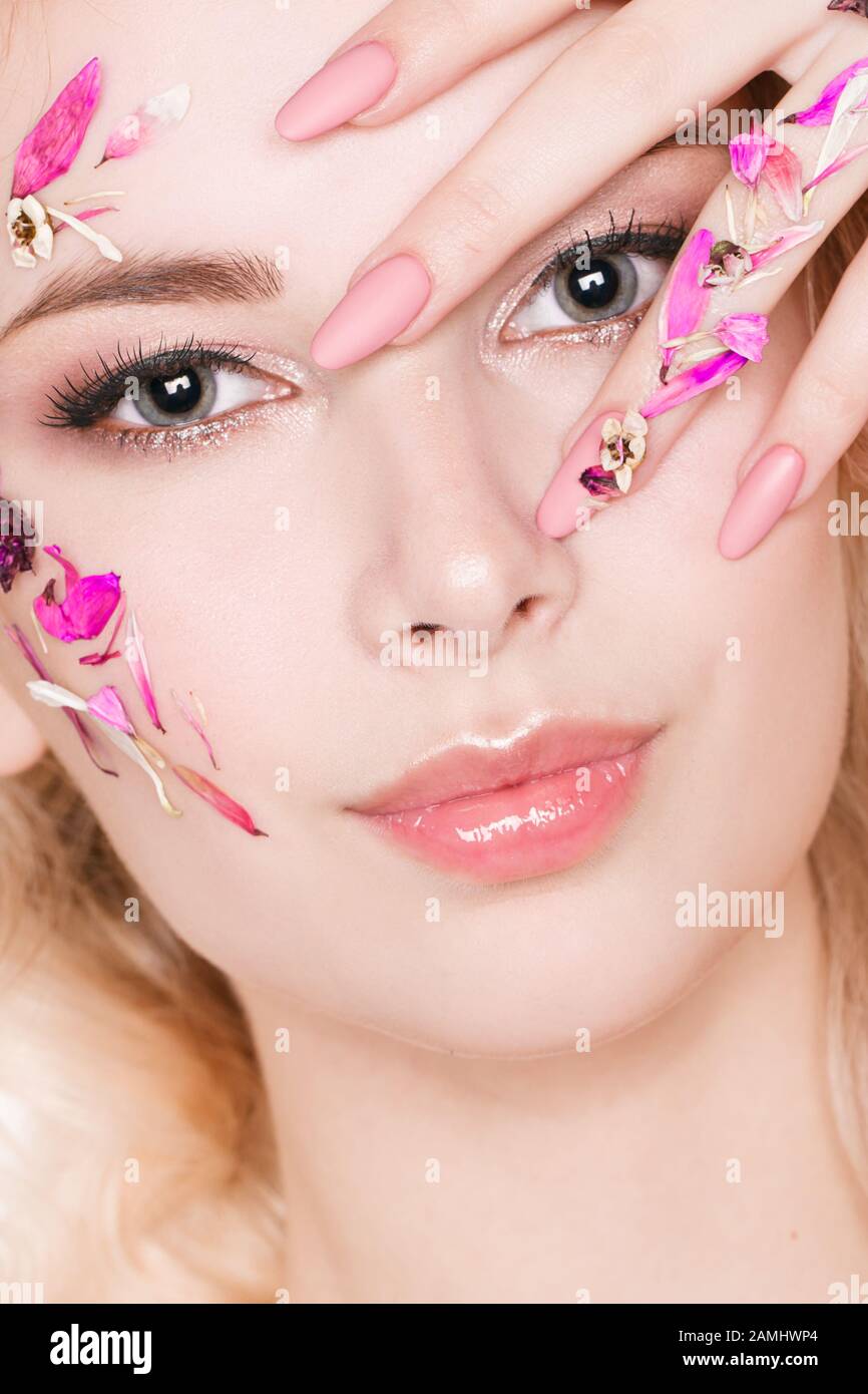 Cosmétiques et manucure. Portrait en gros plan d'une femme attrayante avec des fleurs sèches sur son visage, couleur pastel de la conception de l'ongle, maquillage et peau parfaits Banque D'Images