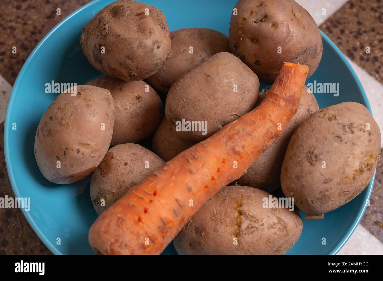 Les pommes de terre et les carottes non pelées se trouvent dans un bol bleu. Légumes bouillis Banque D'Images