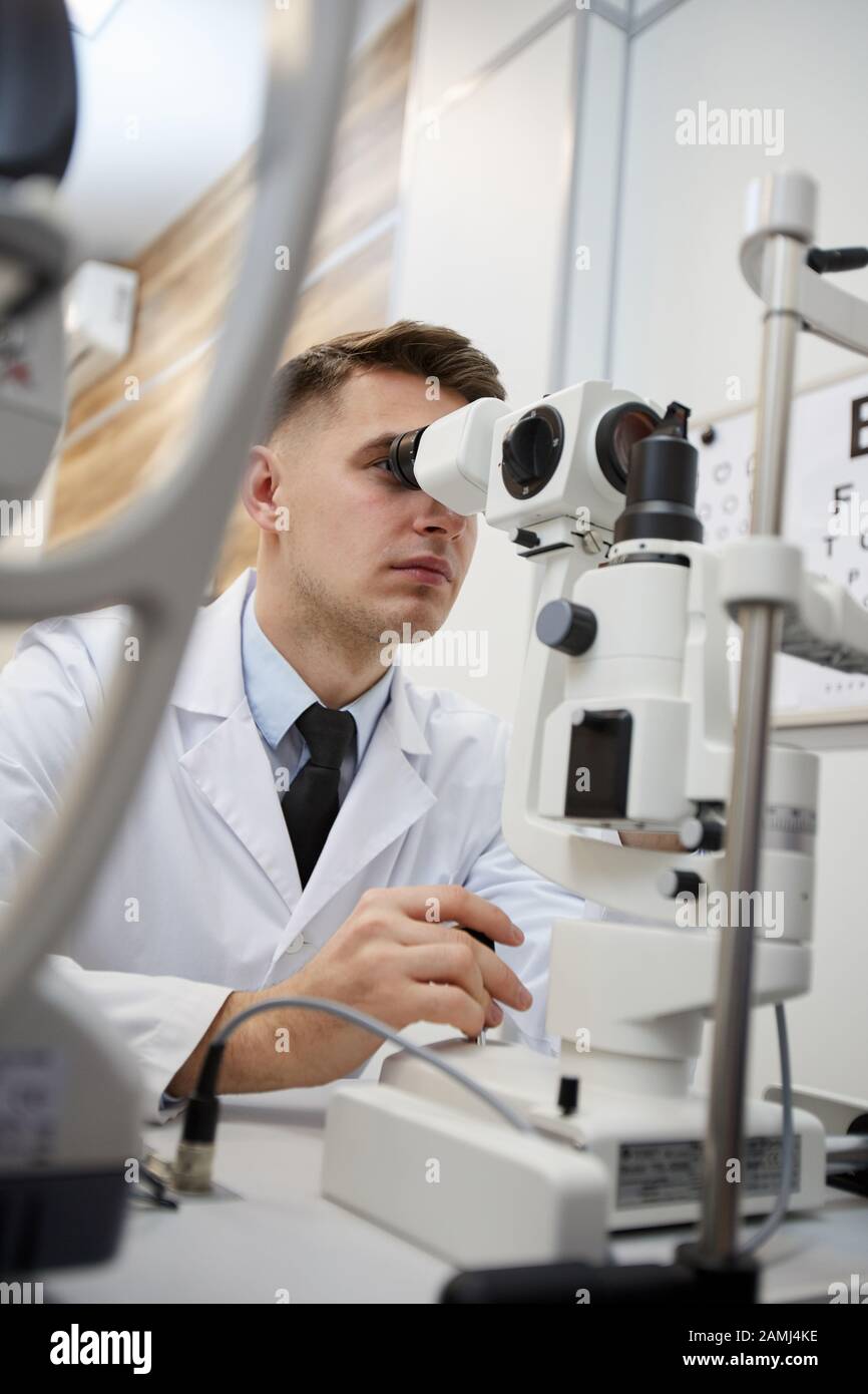 Portrait de l'optométriste masculin à l'aide d'une machine réfractomètre tout en testant la vision d'un patient non reconnaissable Banque D'Images