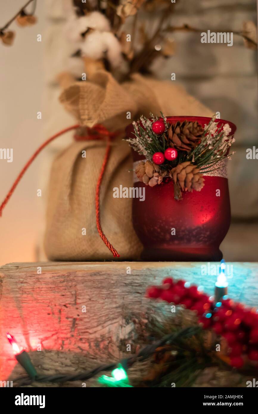 Décorations de Noël assises sur un manteau en cèdre rugueux au-dessus d'une cheminée. Petit pot rouge, baies et décor de burap. Banque D'Images