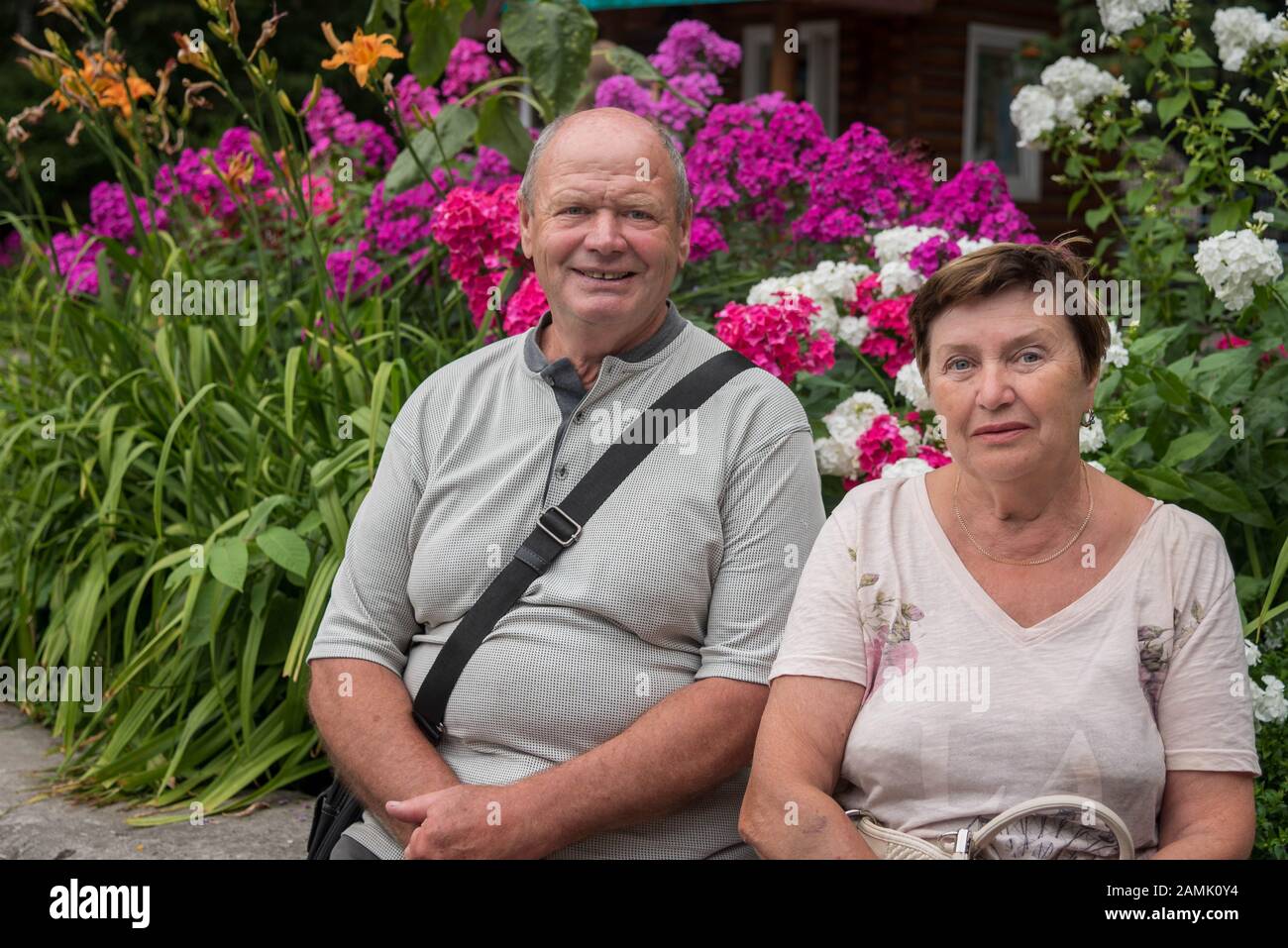 Portrait du couple russe senior dans le parc en Sibérie avec des fleurs lumineuses en arrière-plan. Banque D'Images