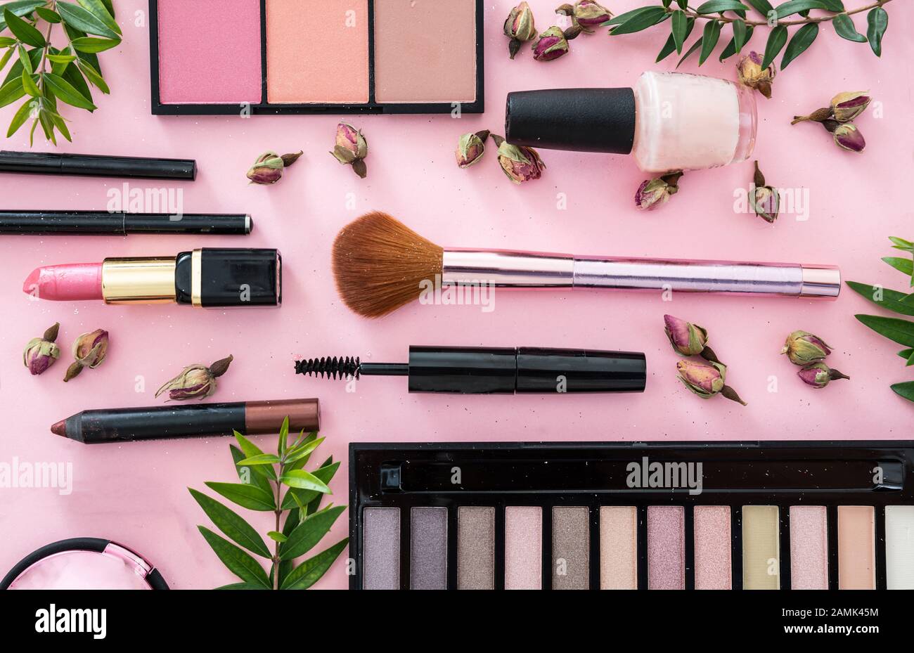 Maquillage cosmétiques naturels plat pose. Rouge à lèvres et vernis à ongles, ombres à paupières et roussettes, brosses, crayons et boutons de roses sur fond de couleur rose. Banque D'Images