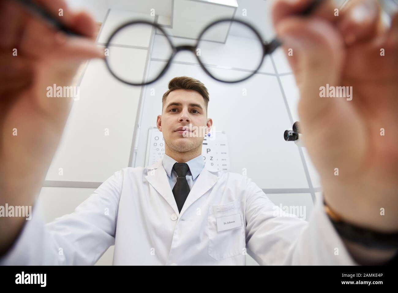 Prise de vue de jeune optométriste mettant des lunettes sur un patient non reconnaissable pendant le test de vision dans une clinique moderne, espace de copie Banque D'Images
