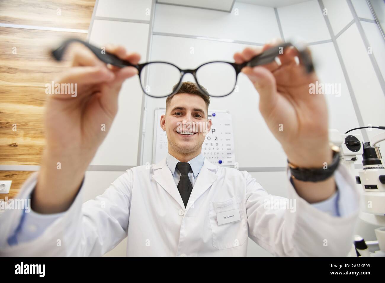 Prise de vue de l'optométriste souriant mettant des lunettes sur un patient non reconnaissable pendant le test de vision dans une clinique moderne, espace de copie Banque D'Images