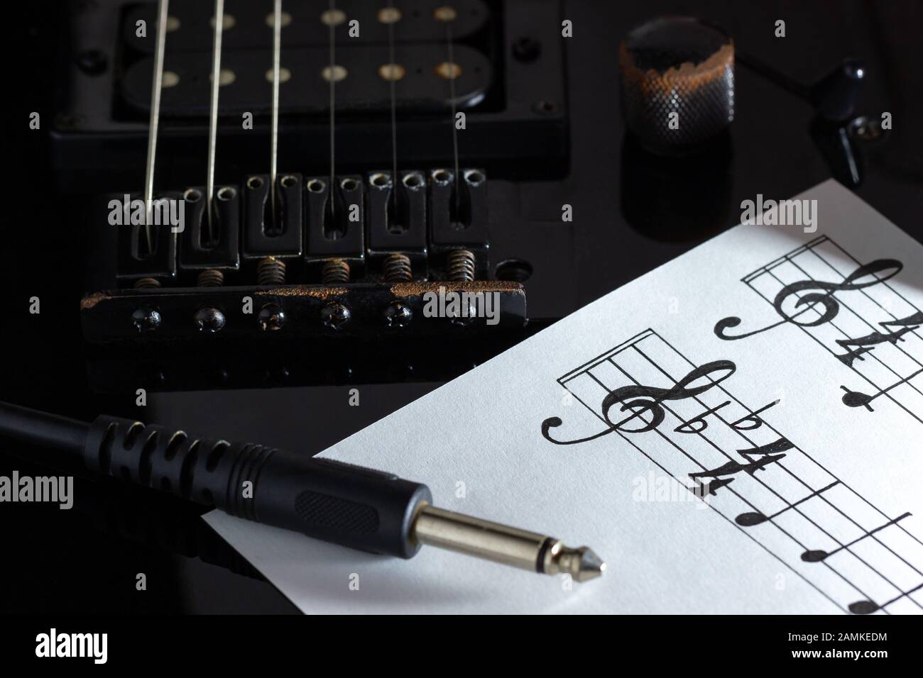 Note de musique et câble jack sur guitare électrique noire dans l'obscurité. Concept de musique rock créative. Banque D'Images