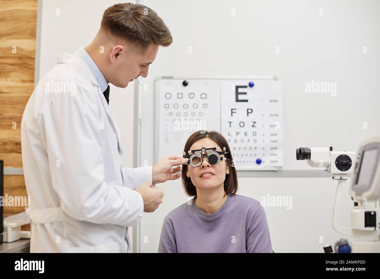 Portrait de l'optométriste homme mettant le cadre d'essai sur le patient féminin pendant l'examen de la vision dans la clinique moderne, espace de copie Banque D'Images
