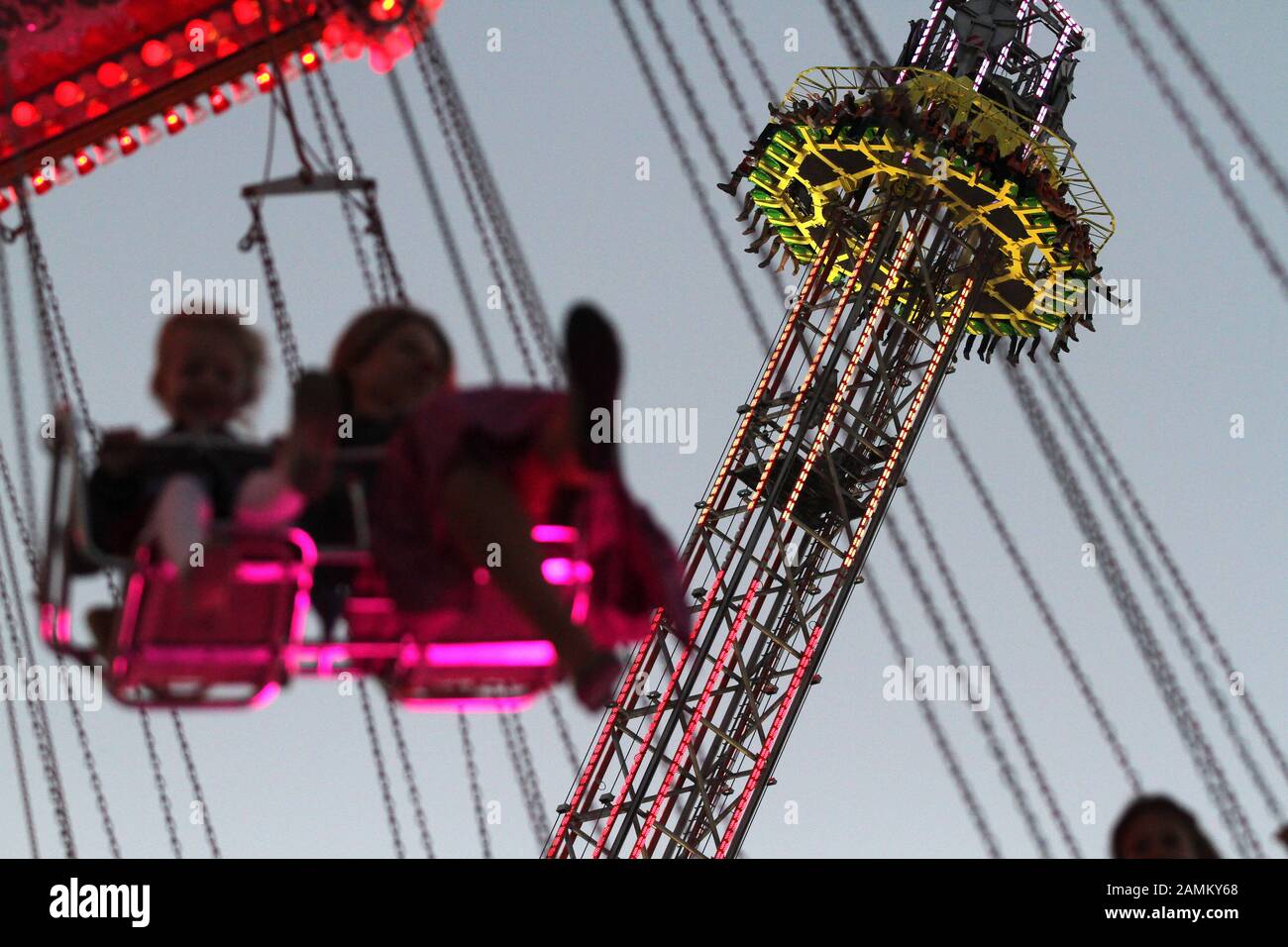 Passagers dans le carrousel à chaînes à la fête de la bière du soir, en arrière-plan la course Free Fall. [traduction automatique] Banque D'Images