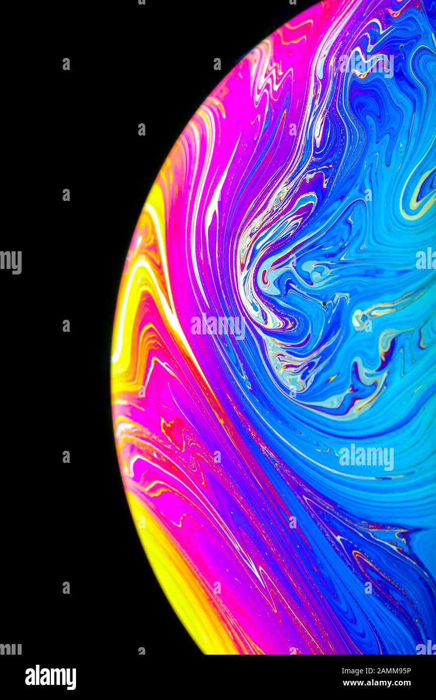 Gros plan sur l'arc-en-ciel psychédélique de couleurs mélangeant et tourbillonnant dans une bulle de savon pour ressembler à une galaxie ou une planète fantasy isolé un fond noir Banque D'Images