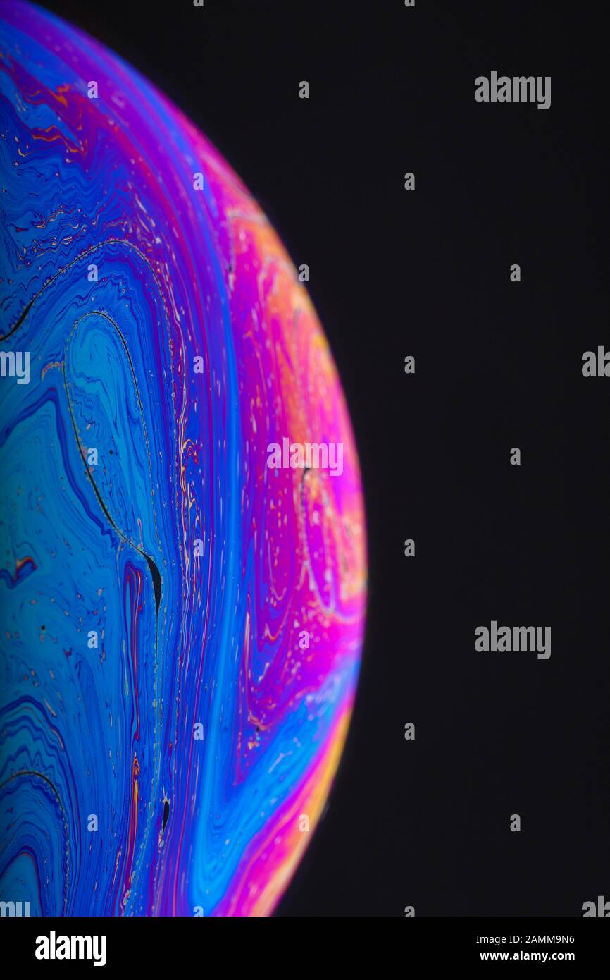Gros plan sur l'arc-en-ciel psychédélique de couleurs mélangeant et tourbillonnant dans une bulle de savon pour ressembler à une galaxie ou une planète fantasy isolé un fond noir Banque D'Images