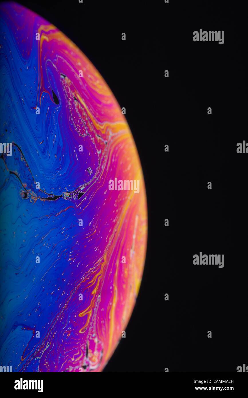 Gros plan sur l'arc-en-ciel psychédélique de couleurs mélangeant et tourbillonnant dans une bulle de savon pour ressembler à une galaxie ou une planète fantasy isolé un fond noir Banque D'Images