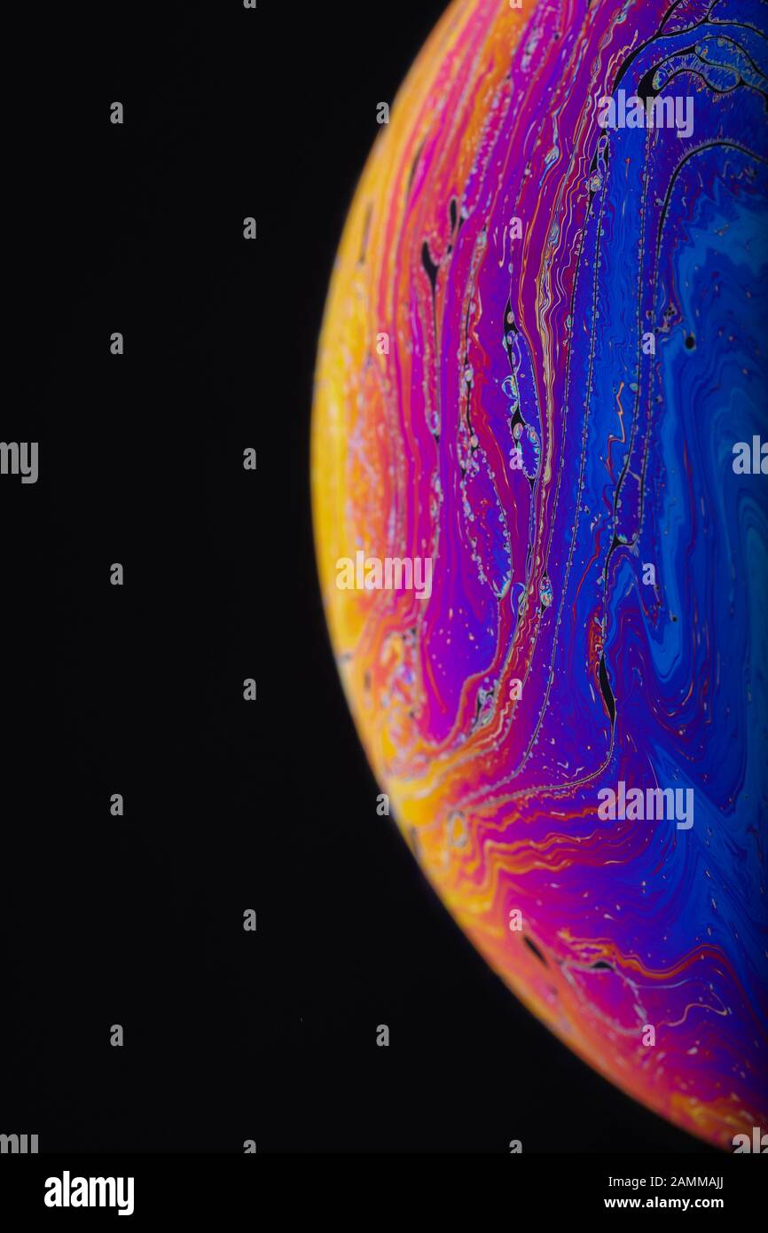 Gros plan sur l'arc-en-ciel psychédélique de couleurs mélangeant et tourbillonnant dans une bulle de savon pour ressembler à une galaxie ou une planète fantasy isolé un fond noir Banque D'Images